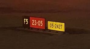 Night photo of a three-panel sign array: a yellow “F5” location panel, a red “23-05” runway designator, and a yellow panel reading “05-2427” with no unit and no arrow.
