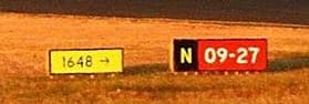 A small yellow panel reading “1648 →” next to a black “N” location panel and a red “09-27” runway designator.