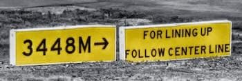 A yellow panel reading “3448M →” using an uppercase M for metres, beside a second yellow sign reading “FOR LINING UP / FOLLOW CENTER LINE”.