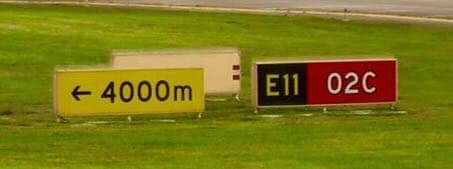 A large yellow panel reading “← 4000m”, then a conspicuous gap, then a black “E11” location panel and red “02C” runway designator.