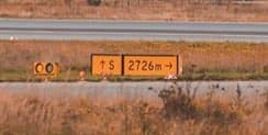 A yellow sign reading “↑ S | 2726m →”, combining a location message with the runway distance.