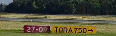 A red “27-09” runway designator beside a yellow panel reading “TORA 750 →”, spelling out TORA but omitting the unit.